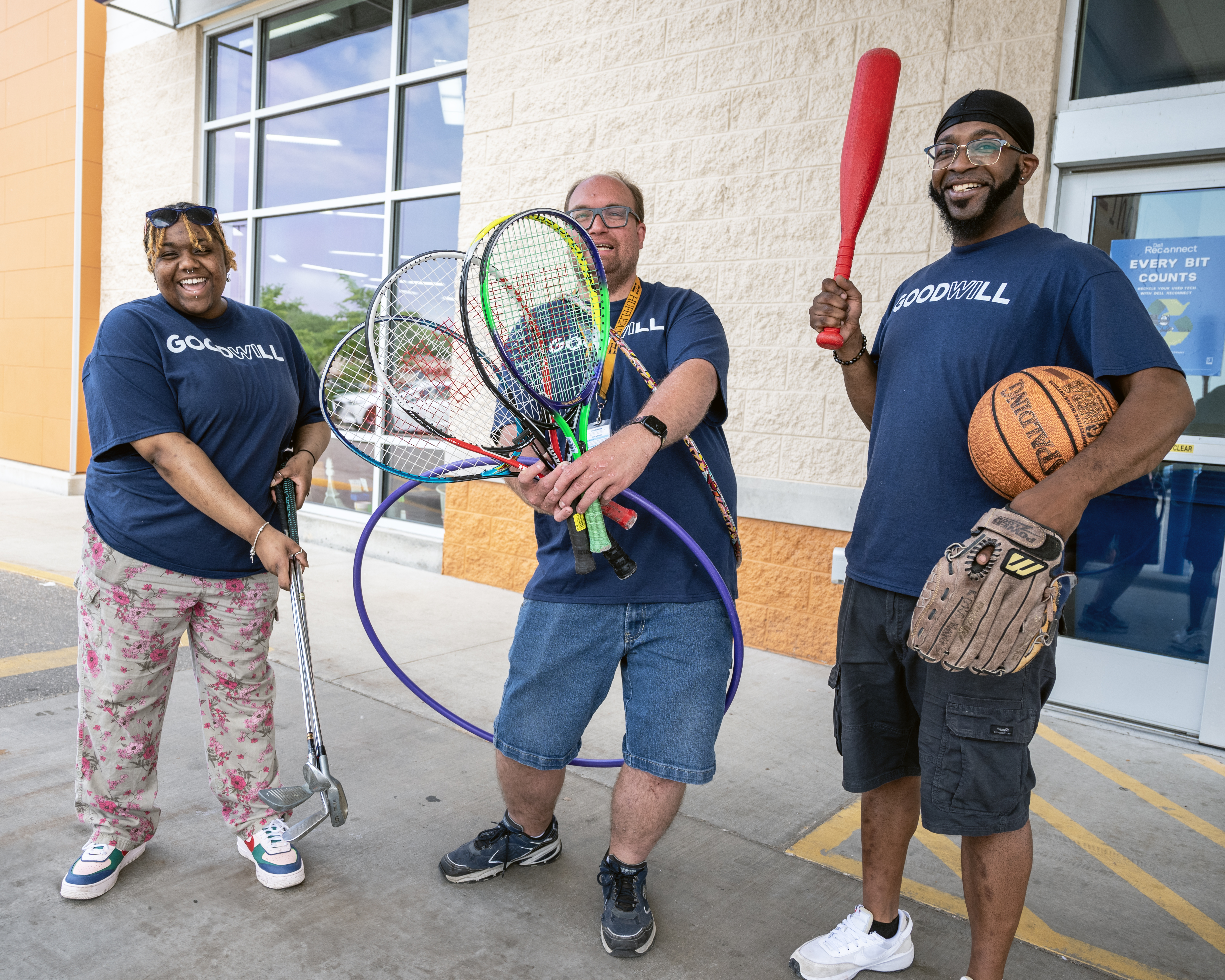 image of Goodwill South Central Wisconsin staff holding outdoor gear: golf clubs, tennis rackets, hula hoop, baseball bat, basketball